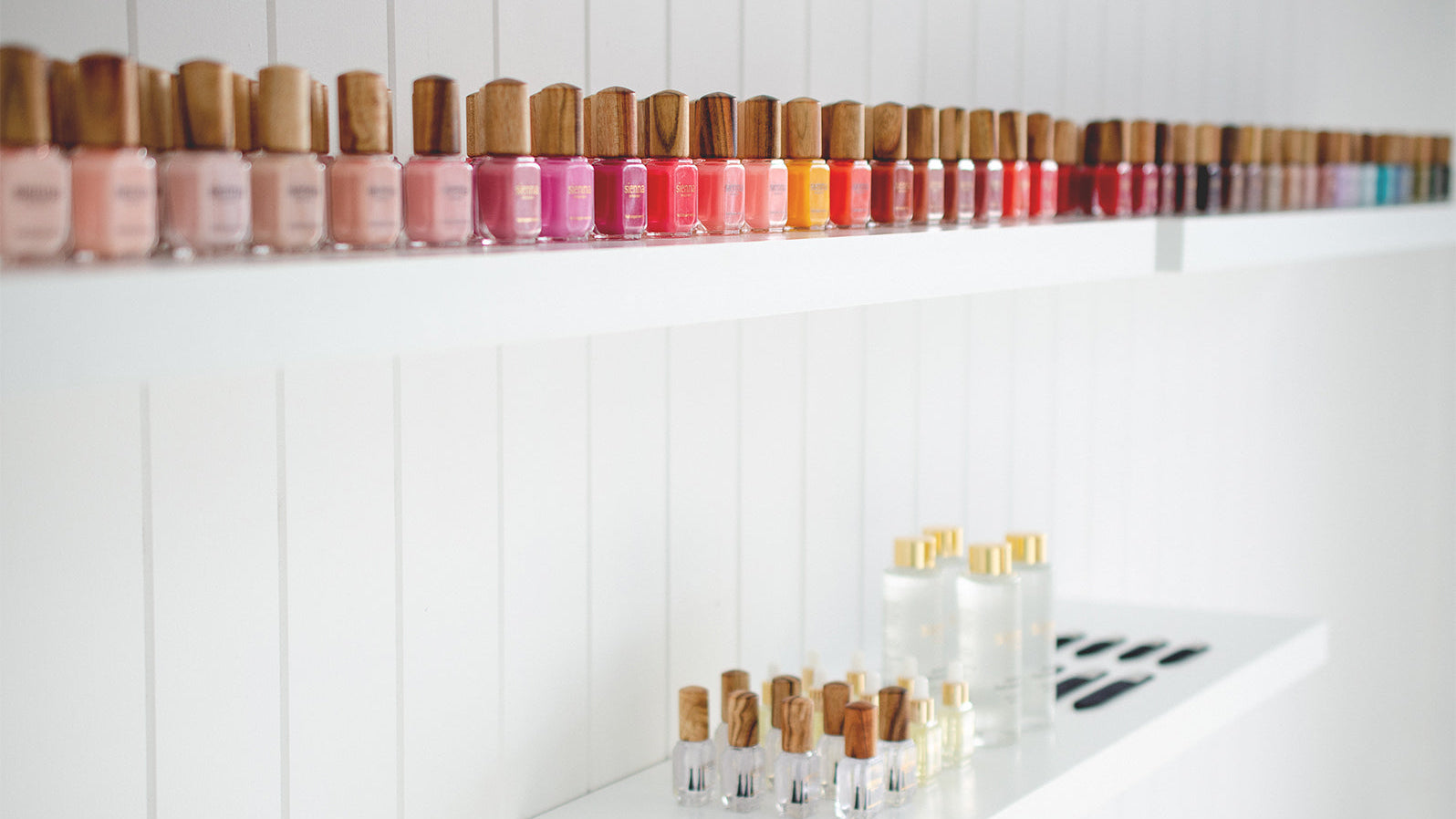 Row of nail polish bottles on a white shelf with a white background